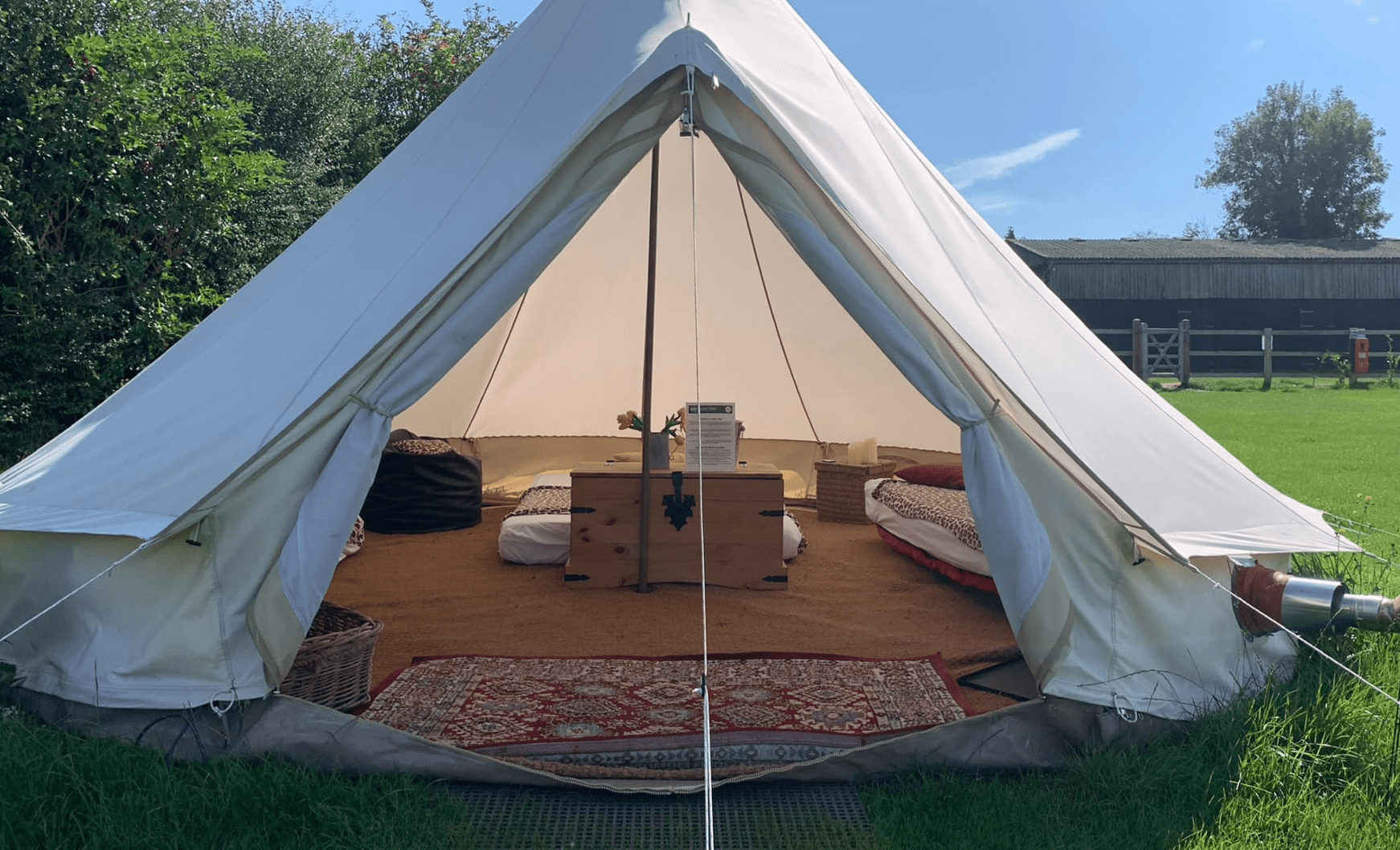 Open white canvas tent on a grassy field with a wooden coffee table, cushions, and a rug inside.