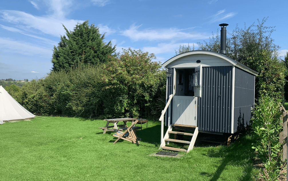 exterior of camping hut in the corner of a field next to a hedgerow