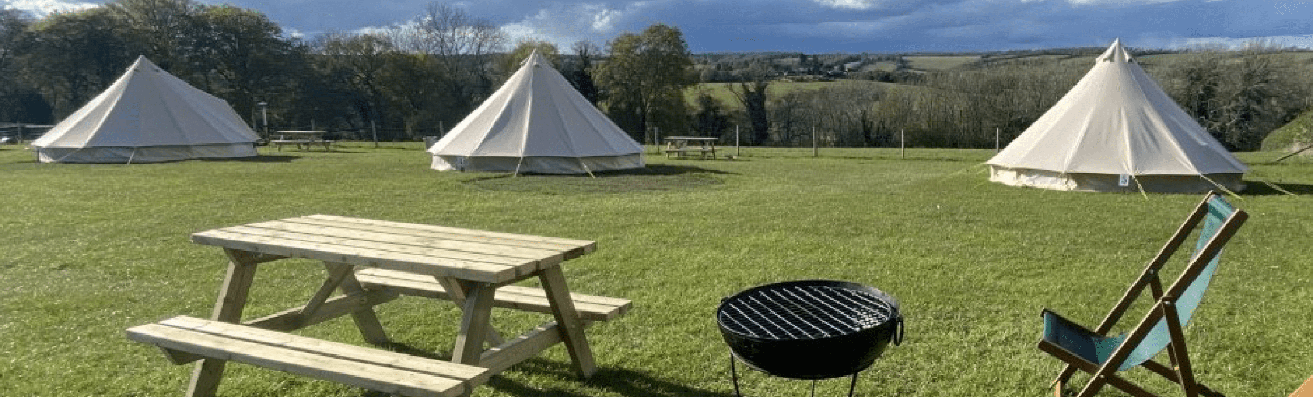 three glamping tents, wooden bench, unlit barbeque and a deck chair
