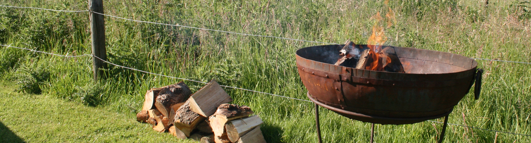 fire pit with logs burning and a pile of logs beside it