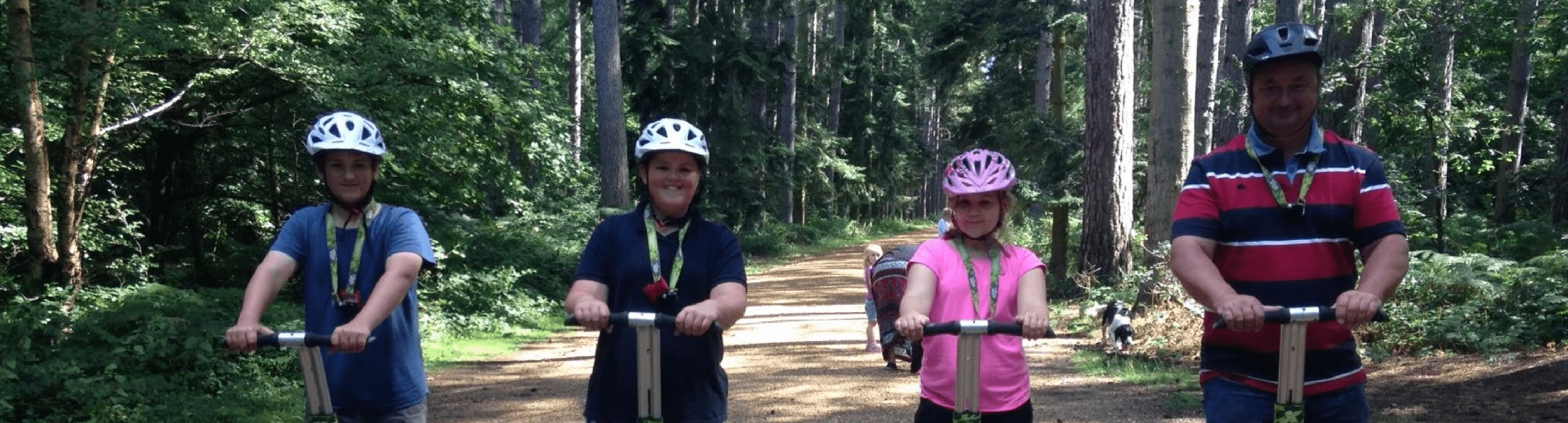 three children and a guardian riding Segway's wearing helmets in the forest