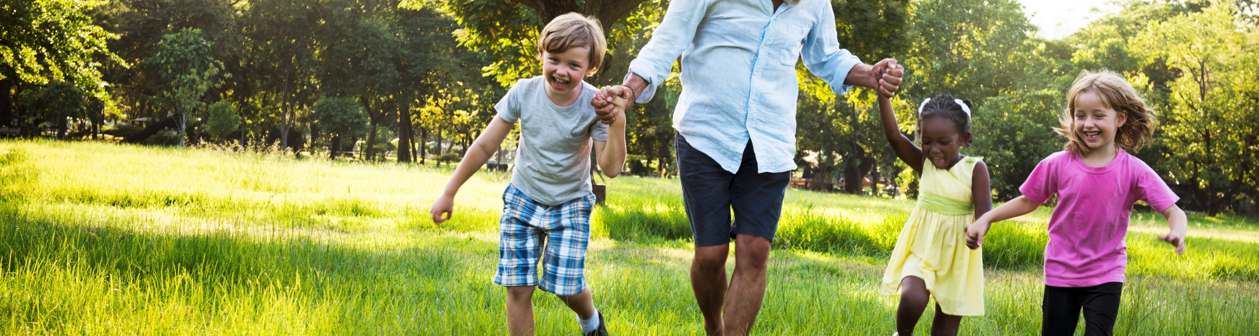 three children and a guardian playing in a field with long grass and trees in the background