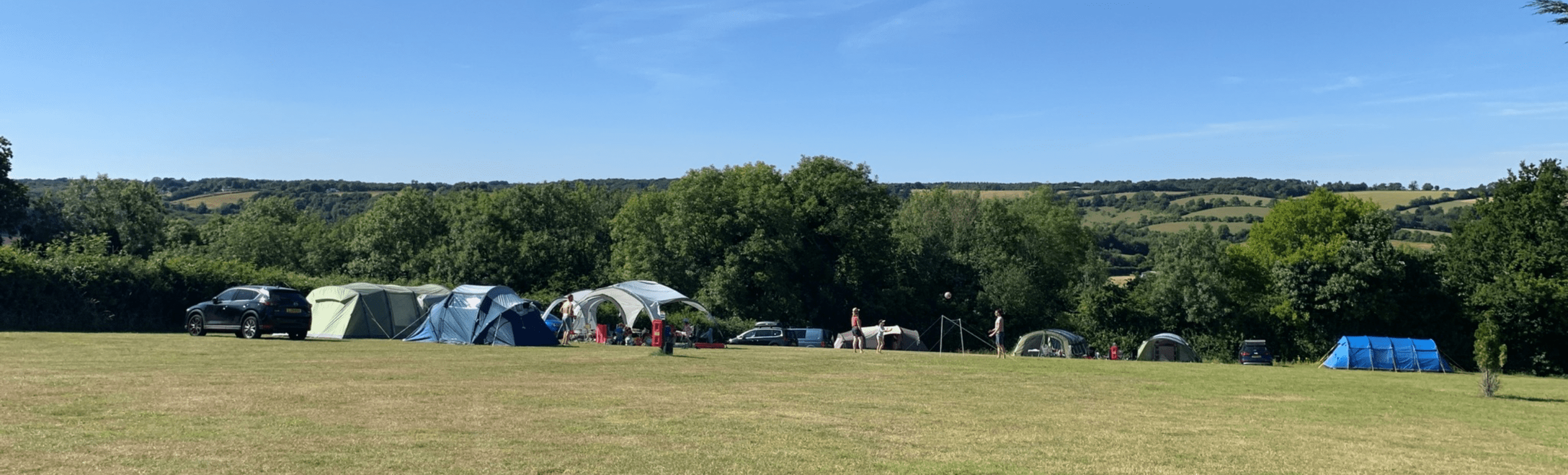 camping field with multiple tents, cars, and campers with a view of the rolling countryside hills in the background