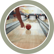 A bowler releases an orange bowling ball down the lane toward the pins in a bowling alley.