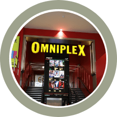 Omniplex cinema entrance with a bright yellow sign above a red-lit doorway and a poster display.