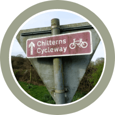 Chilterns Cycleway sign with a bicycle icon on a metal post in a wooded area.