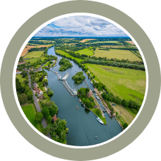 Aerial view of a winding canal through lush green farmland with trees and several boats on the water.
