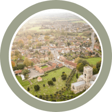 Aerial view of Thame with red-roofed buildings, green fields, and a church tower.
