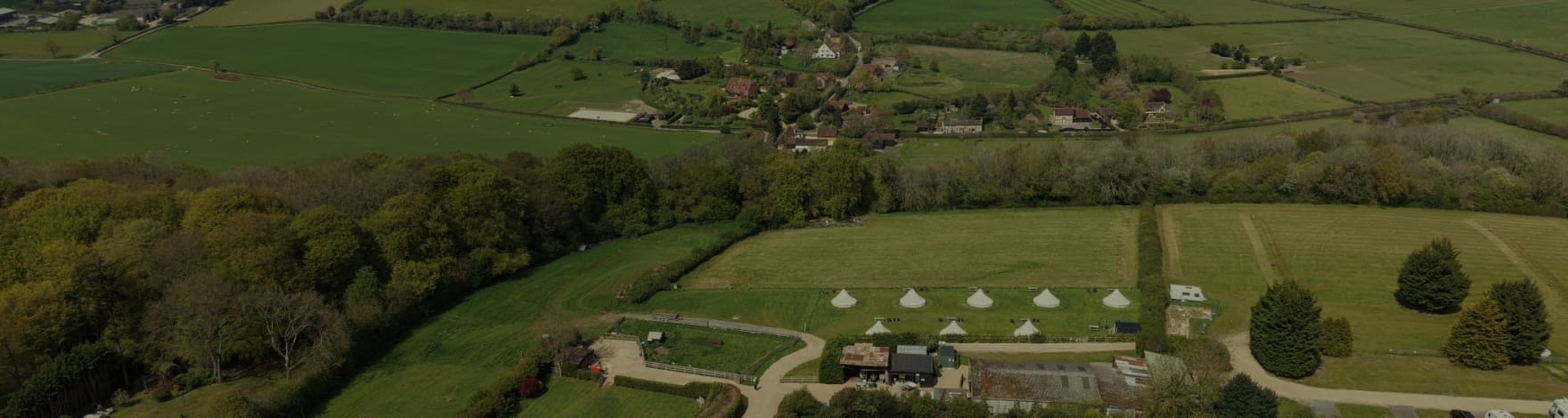 Aerial view of a rural countryside with green fields, hedgerows, and a cluster of farm buildings arranged around a central courtyard.